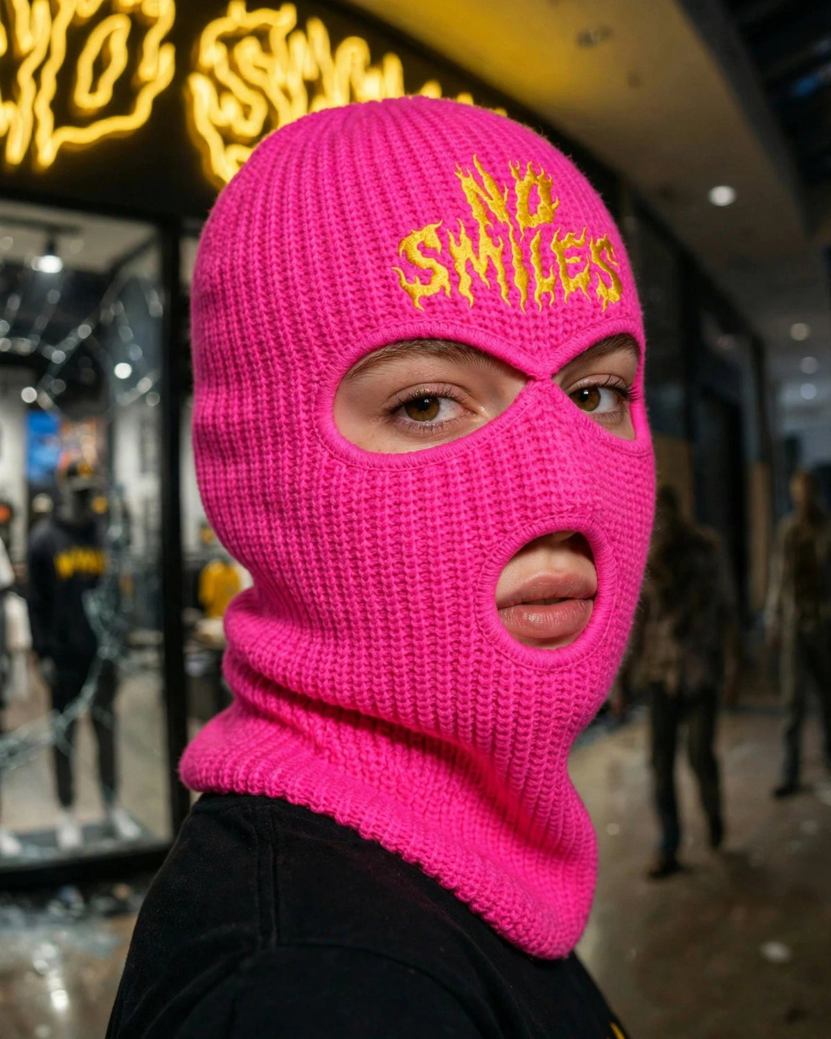 Pink 3-hole ski mask with yellow No Smiles embroidery worn in front of the No Smiles store, three-quarter view