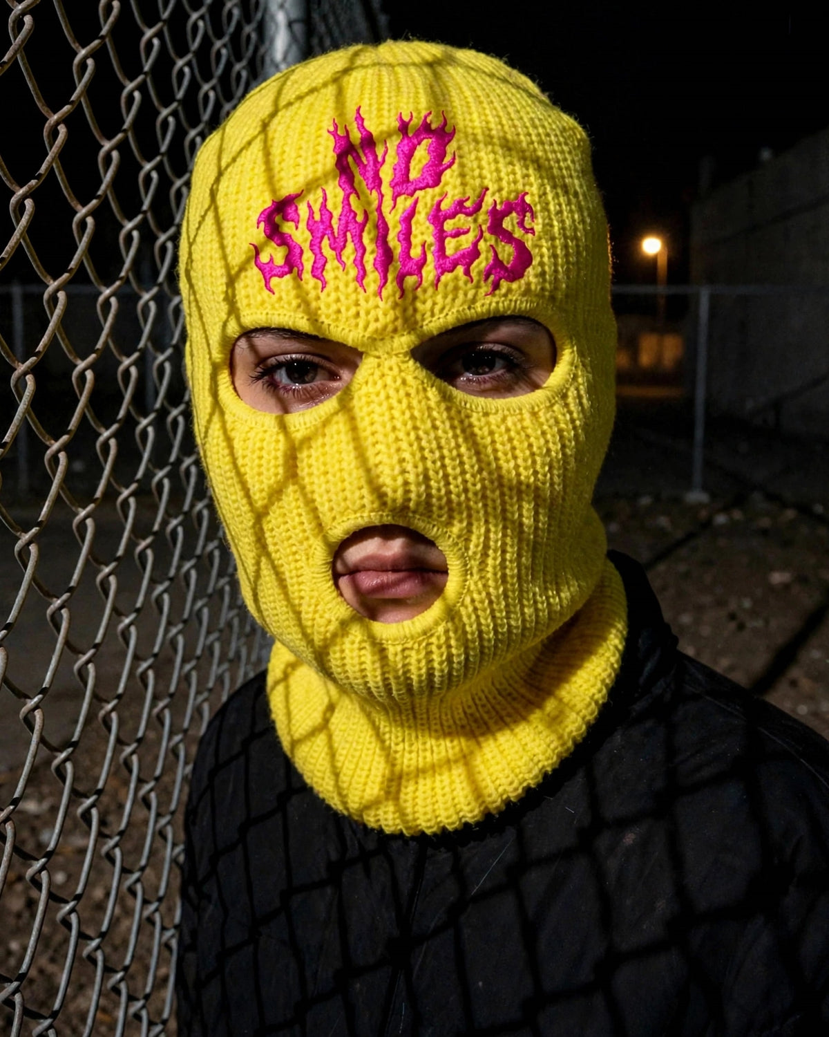 Yellow No Smiles ski mask, chain-link fence
